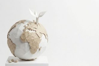 Artystyczna instalacja przedstawiająca globus wykonany z białego i brązowego papieru techniką origami. Z górnej części kuli ziemskiej wyrasta mała, biała papierowa roślina z dwoma listkami, symbolizująca ekologię i zrównoważony rozwój w przemyśle papierniczym.