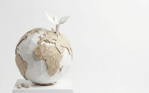 Artystyczna instalacja przedstawiająca globus wykonany z białego i brązowego papieru techniką origami. Z górnej części kuli ziemskiej wyrasta mała, biała papierowa roślina z dwoma listkami, symbolizująca ekologię i zrównoważony rozwój w przemyśle papierniczym.
