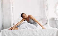 Młoda kobieta rozciągająca się na wygodnym łóżku z materacem premium w jasnej sypialni z białą cegłą.