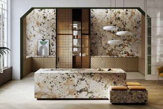 Luksusowa kuchnia z monolityczną wyspą i ścianami wykończonymi wielkoformatowym spiekiem kwarcowym Alpinus White o wyrazistym, kamiennym wzorze w odcieniach bieli, beżu i czerni. Dolne szafki posiadają fronty z pionowym ryflowaniem w kolorze piaskowym, a całość dopełniają nowoczesne, obłe lampy wiszące oraz eleganckie detale z drewna i plecionki wiedeńskiej.