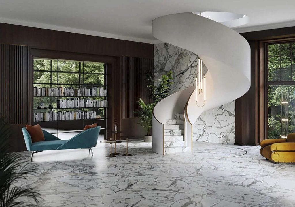 Przestronny, luksusowy hol z imponującymi kręconymi schodami, których stopnie oraz przylegająca ściana i podłoga zostały wykończone spiekiem kwarcowym Invisible White o wzorze klasycznego, szarego marmuru. Aranżację uzupełniają ciemne, drewniane panele ścienne z lamelami, designerska niebieska szezlong oraz żółty fotel, a duże przeszklenia otwierają widok na zieleń ogrodu i biblioteczkę.