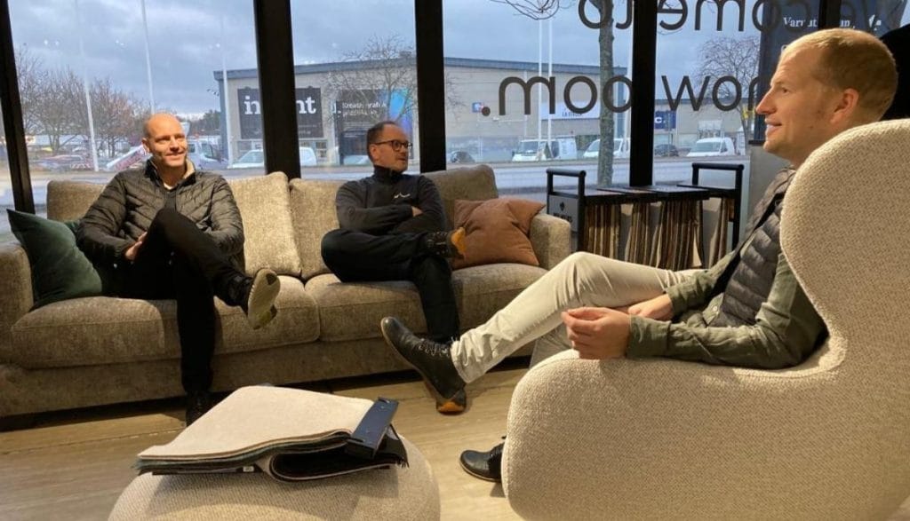Trzech mężczyzn rozmawiających w strefie wypoczynkowej – mobilny showroom z nowoczesnymi meblami.