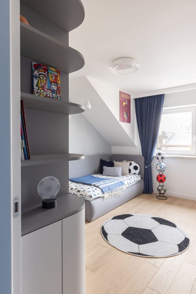 Pokój młodego fana piłki nożnej na poddaszu domu na warszawskim Zaciszu, autorstwa JLW Studio. Architekt Joanna Lemka-Wójcik idealnie wpisała geometryczną, szarą zabudowę meblową w trudne skosy. Fot. Pion Poziom.