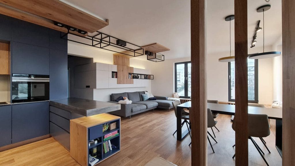 Około 100-metrowy apartament w nowo wybudowanej plombie w centrum Krakowa. W połączonej przestrzeni dziennej (wejście / kuchnia / jadalnia / salon) architekci musieli zmierzyć z niecodziennym wyzwaniem: drzwi wejściowe do mieszkania umieszczone… bezpośrednio w kuchni. Jedynym rozwiązaniem było symboliczne oddzielenie zabudowy lodówki od drzwi kilkoma ażurowymi panelami z drewna dębowego. Naturalny dębowy fornir w połączeniu ze zgaszonym, matowym granatem to zestawienie narzucone przez inwestorów. Inwestorzy mieli dużo wątpliwości co do blatów z nierdzewnej stali, jednak pierwsze obawy szybko zastąpił zachwyt nad trwałością, praktycznością i pięknem delikatnie szlifowanego metalu. Projekt i realizacja: Swałtek Design Studio.
