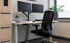 Nowoczesne stanowisko pracy z ergonomicznym biurkiem o regulowanej wysokości, dwoma monitorami na ramieniu, czarnym krzesłem siatkowym i szafką na dokumenty z wbudowanym tabletem.