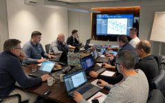 Zdjęcie spotkania biznesowego, na którym zespół ekspertów analizuje modele 3D i dane techniczne na ekranach laptopów i monitorze ściennym w ramach projektu wdrożenia systemu Imos.