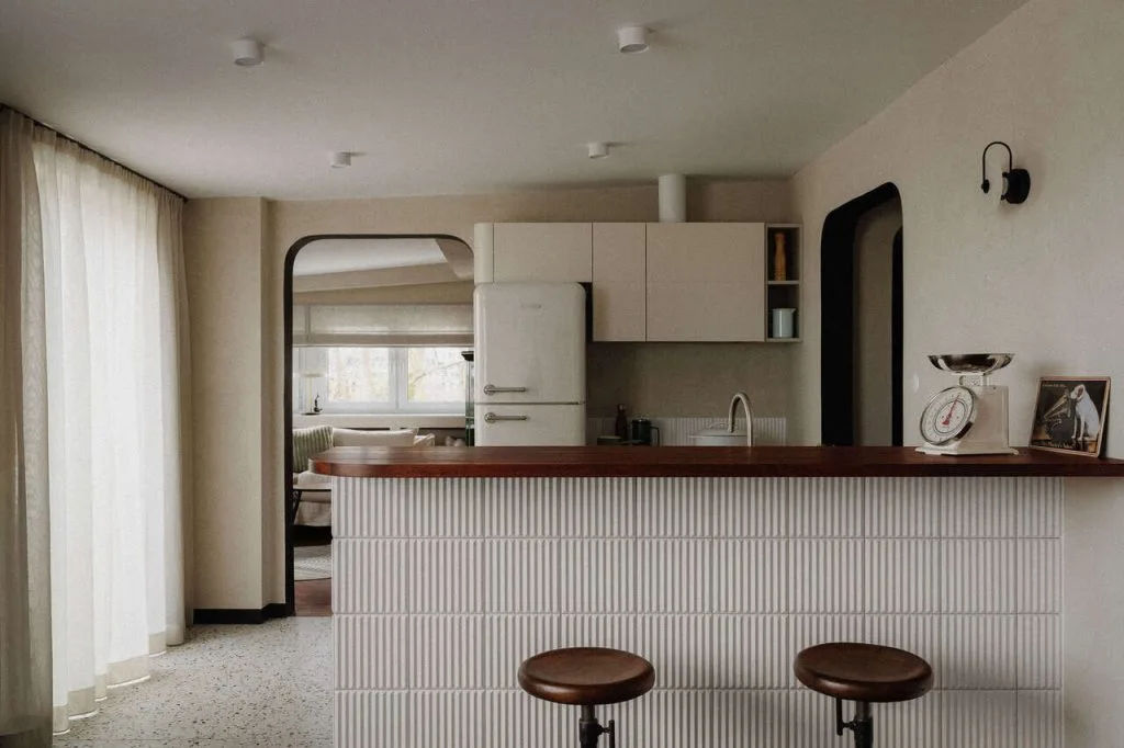 Apartament na ostatniej kondygnacji modernistycznej kamienicy w Gdyni. Ściany pokryto tynkiem strukturalnym, podłoga to parkiet przemysłowy. Dominują naturalne materiały, trochę retro: lastryko, ryflowane kafle, len, tapety obiektowe. Do tego dochodzą – jako akcenty – mocne kolory i wzory, np. zielony kominek. To wnętrze spokojnie, a jednocześnie odważnie. Proj. Ossowska. architektura wnętrz. Zdjęcia  - FotoMohito.