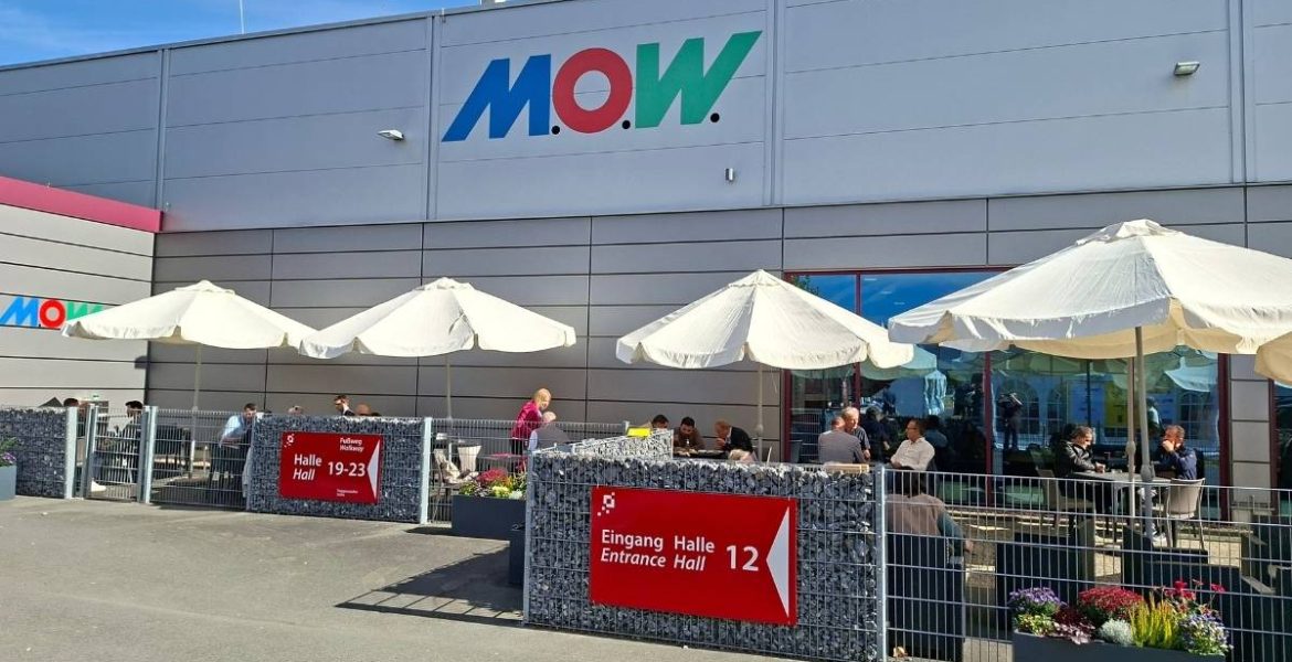 Wejście do Hali 12 na targach M.O.W. 2026 z widocznym logo M.O.W. i ogródkiem kawiarnianym.