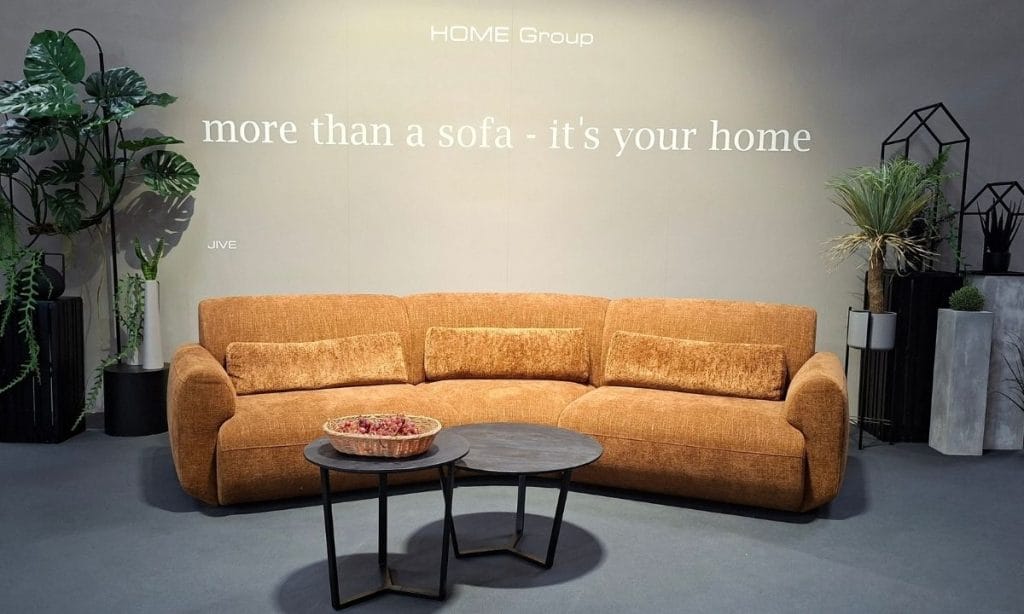 Nowoczesna miodowa sofa tapicerowana z okrągłymi stolikami kawowymi na stoisku Home Group na M.O.W. 2026.