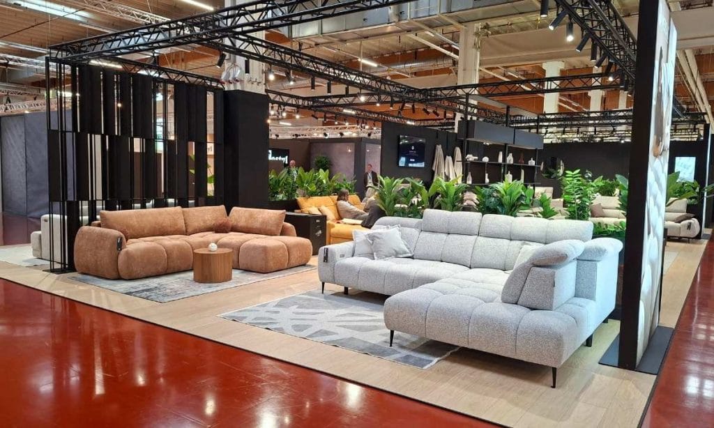 Jasnoszary narożnik oraz rudobrązowa sofa na stoisku ekspozycyjnym Wersal na M.O.W. 2026.